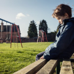 Upset problem child sitting on play park playground bench concept for bullying, depression, child protection or loneliness Upset problem child sitting on play park playground bench concept for bullying, depression, child protection or loneliness