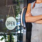 The woman is a waitress in an apron, the owner of the cafe stands at the door with a sign Open waiting for customers. Small business concept, cafes and restaurants The woman is a waitress in an apron, the owner of the cafe stands at the door with a sign Open waiting for customers. Small business concept, cafes and restaurants
